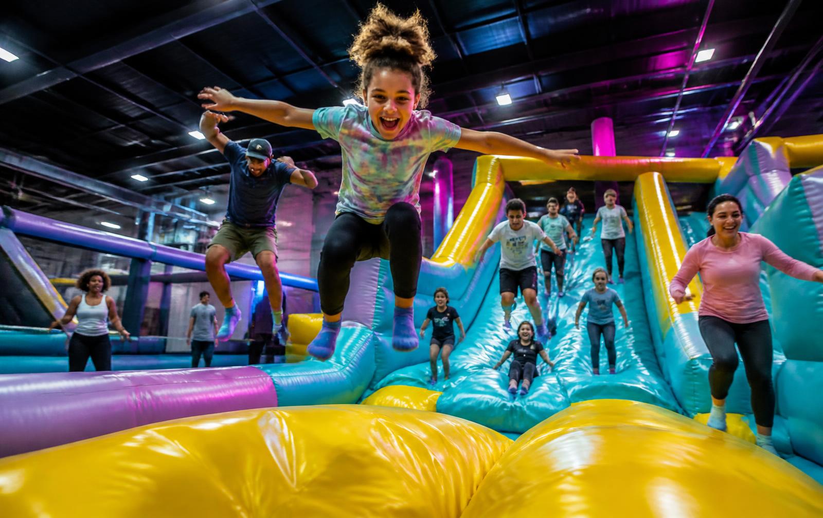 Children, teenagers and adults jumping across a colourful indoor inflatable park